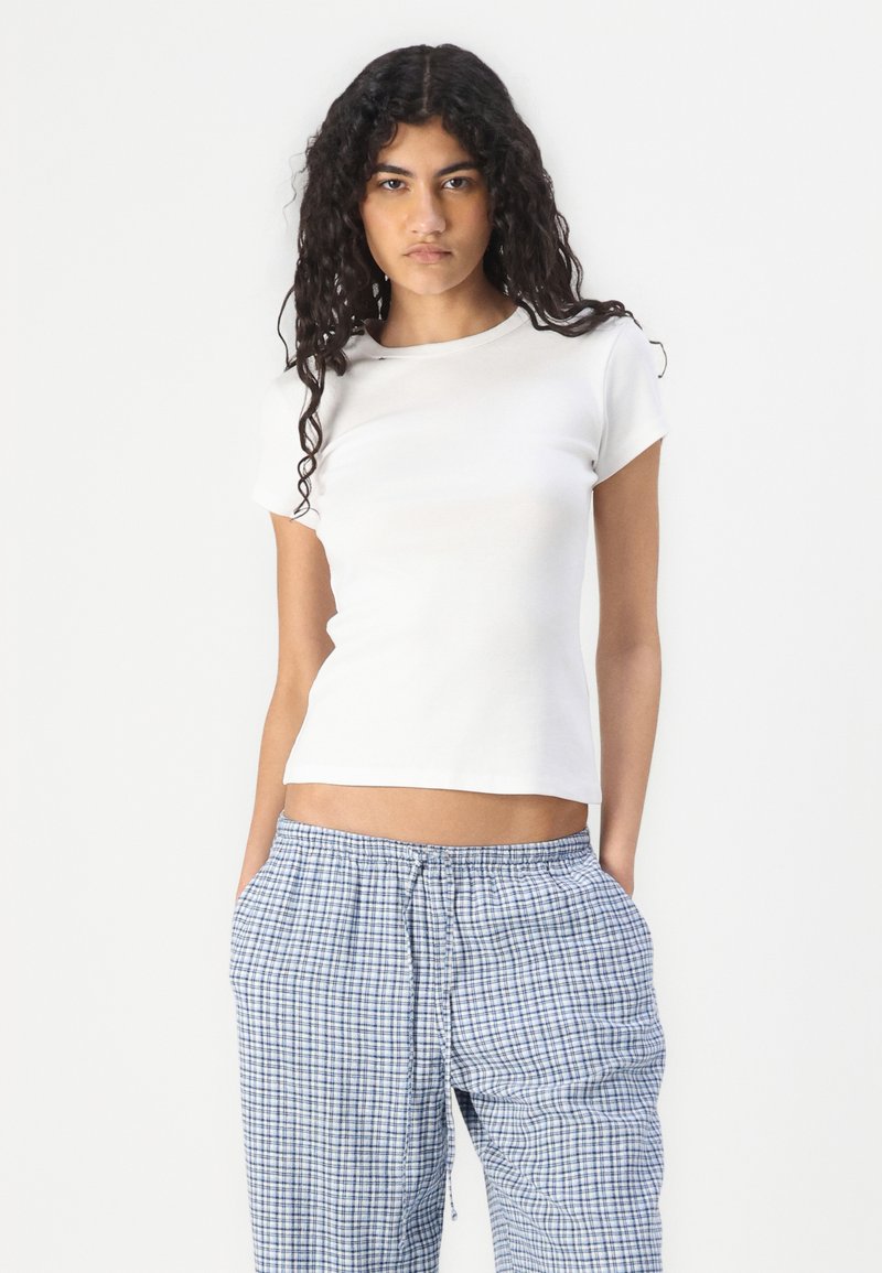 Biała, dopasowana koszulka z krótkim rękawem, w połączeniu z niebieskimi i białymi spodniami w kratę na sznurki. Materiał wygląda na gładki i lekki.