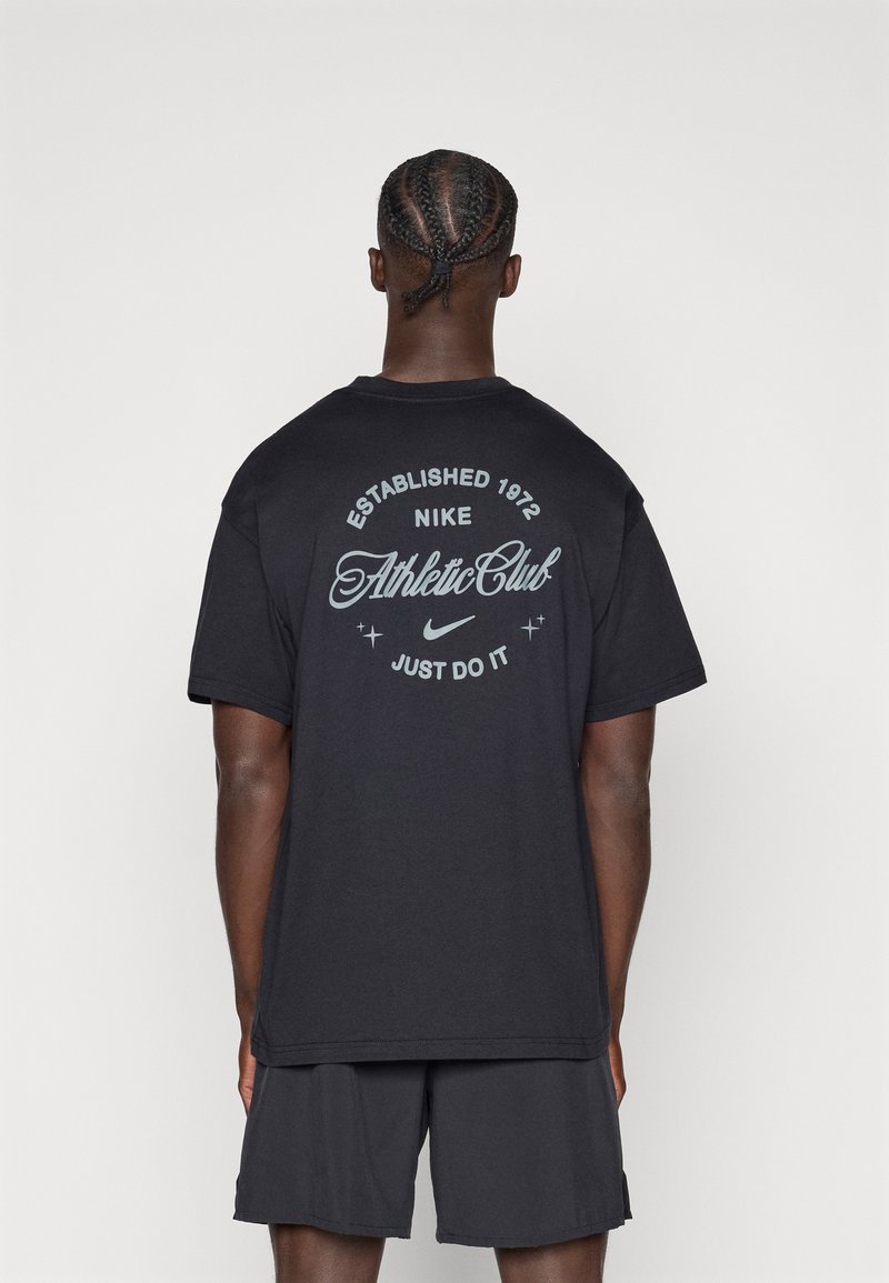 Μαύρο t-shirt Nike με τη φράση "Established 1972" και "Athletic Club" σε διακοσμητική λευκή γραμματοσειρά. Συνδυάζεται με γκρι σορτς.