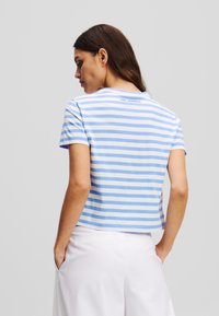 T-shirt à manches courtes rayé en coton bleu et blanc, avec un col rond et un logo dans le dos. Coupe décontractée, style court.