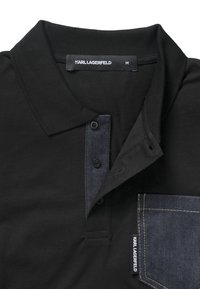 Černé polo tričko s džínovým límcem a kapsou, se čtyřmi knoflíky a tkanou značkovou štítkem. Měkká bavlněná textura. Velikost M.