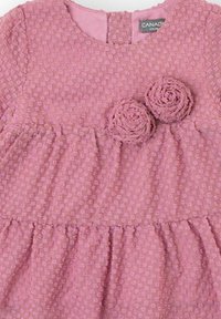 Vestido rosa con tela texturizada, mangas cortas y dos adornos florales en el corpiño. Cintura fruncida y falda acampanada. Cierre con botones en la parte trasera.