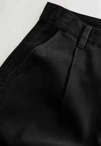 Sorte denimbukser med en struktureret talje, skrå sidelommer og en glat tekstur med subtile syninger.