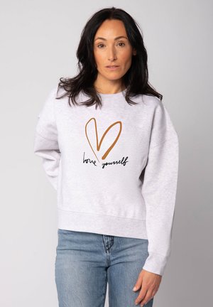 Lichtgrijze sweatshirt met een relaxte pasvorm, voorzien van een bruine hartgrafiek en de tekst "hou van jezelf" in het zwart. Zachte textuur, geribbelde manchetten.