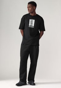 Black graphic t-shirt featuring a white 'Joy Division' design, paired with black loose-fitting trousers and black athletic shoes.