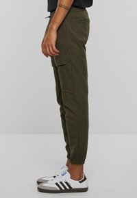 Olijfgroene cargobroek met elastische enkels, zijzakken en een trekkoord in de taille; gecombineerd met witte en grijze sneakers.