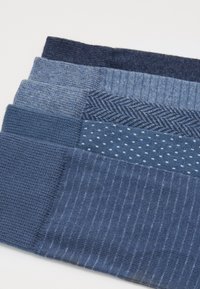 Set of four socks in varying shades of blue, featuring patterns like stripes, dots, and herringbone. Made of a soft, textured knit material.
