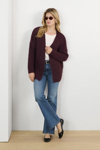Burgundy, textured cardigan over a white top, paired with blue flared jeans and black flats. Accessories include round sunglasses.