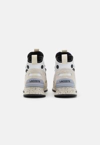 Białe i beżowe sneakersy z fakturowaną, nakrapianą podeszwą. Posiadają czarne akcenty, sznurowany design oraz pętelkę z tyłu.