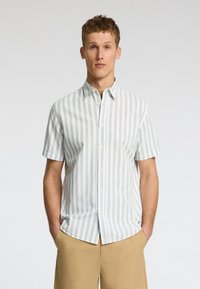 Camisa de manga corta, abotonada, en rayas verticales verde claro y blancas. Hecha de un tejido ligero con un cuello clásico y botones sutiles.