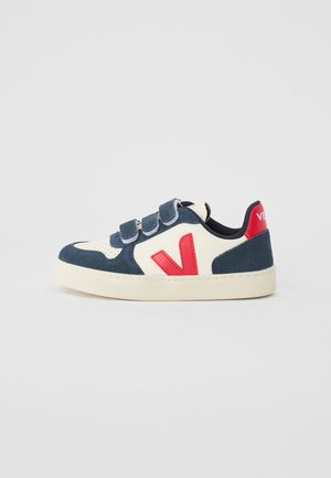 White and navy sneaker with red accents, suede and leather materials, rounded toe, three velcro straps, and logo on heel.
