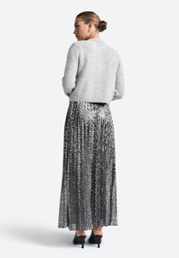 Hallide hallitusseente valmistatud hall lühike kampsun, mis on ühendatud pika, hõbedase, sädeleva plisseeritud seeliku ja mustade kõrgete kontsadega kingadega, mis täiendavad komplekti.