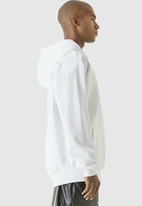 White hoodie with a relaxed fit, large hood, front kangaroo pocket, ribbed cuffs, and hem. Smooth texture, minimalistic design, no patterns.