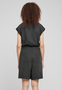 Rompers noirs à manches courtes avec une coupe décontractée, une ceinture élastique et deux poches à l'arrière. Le tissu semble lisse avec une finition mate.