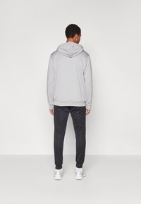 Svetlo siva kapuca s vezicom za kapu, elastičnim rukavima i rubom; uparen s tamnosivim trenirkama i bijelim atletskim cipelama.