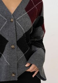 Graue Strickjacke mit einem Rautenmuster in Burgunderrot, Schwarz und Weiß. Verfügt über einen V-Ausschnitt, fünf braune Knöpfe und gerippte Bündchen. Weiche Textur.