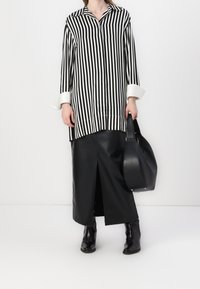 Camisa de rayas en blanco y negro con cuello, de corte holgado y mangas largas, combinada con una falda de cuero negro y botas de tobillo. Sostiene un bolso negro.