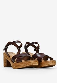 Sandalias de plataforma de cuero marrón con tiras cruzadas, talón descubierto y un tacón de bloque de madera texturizada. Plantilla suave con detalle del logotipo.