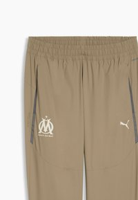 Μπεζ αθλητικό παντελόνι με ελαστική μέση, διακοσμημένο με λευκά λογότυπα και πλαϊνές τσέπες. Το ύφασμα φαίνεται λείο και ελαφρύ.