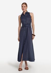 Marinblå ärmlös knäppt klänning med knytmidja, lång silhuett och sidoöppning. Tillverkad av lättviktig tyg med en slät textur.