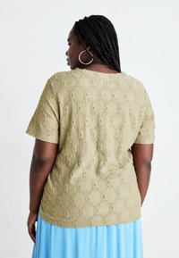 Olive green short-sleeve top featuring a textured, diamond-patterned knit with decorative holes, worn with a light blue skirt.
