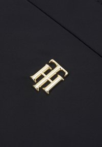Tessuto nero con un logo dorato lucido che presenta lettere intrecciate, centrato sul materiale, con una texture liscia.
