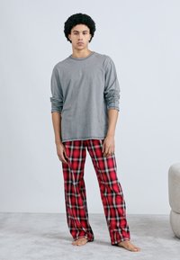 Gray long-sleeve shirt with rolled sleeves paired with red plaid pajama pants featuring black and white accents; model standing barefoot on soft surface.