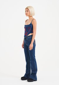 Denim crop-top med rød blomsterbroderi, parret med mørkeblå flared jeans. Modellen bærer sorte platform-sko. Glat tekstur hele vejen igennem.