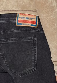 Czarne dżinsy z denimu z widoczną tylną kieszenią, z brązową skórzaną metką oznaczoną "Diesel Industry" z niebieskimi i czerwonymi akcentami.