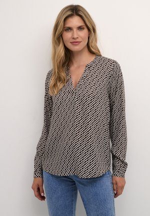 Blusa a maniche lunghe bianca e nera con un motivo, dotata di scollo a V, realizzata in un tessuto leggero e con un taglio morbido. Sotto sono indossati jeans blu.