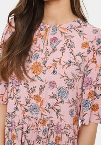 Blommig klänning med en rosa bakgrund och blå och orange blommor, korta ärmar, en nyckelhålsringning och en draperad nederkant.