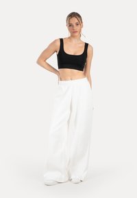 Top corto nero con spalline larghe abbinato a pantaloni bianchi larghi. Il tessuto appare liscio con una silhouette rilassata e drappeggiata.