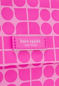 Borsa tote rosa con un motivo di grandi cerchi e rettangoli, con un'etichetta bianca che recita "kate spade NEW YORK" cucita su di essa.