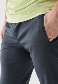 Donkergrijze sportbroek gemaakt van een gladde, rekbare stof; uitgerust met een geperforeerde zijzak en een subtiele logo-accent.
