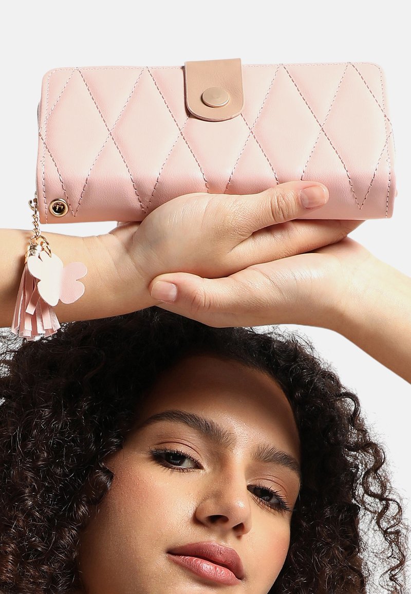 Quilted rosa plånbok med en beige tryckknapp, som har en guldfinish och en rosa tofs med en fjärilsdetalj.