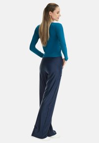 Long-sleeve teal top paired with navy wide-leg pants. The outfit features smooth fabric and a fitted silhouette. White shoes complete the look.