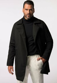 Abrigo largo negro con cuello muesca, botones frontales y bolsillos laterales, superpuesto a un jersey de tortuga negro, combinado con pantalones de color claro.