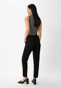 Schwarze maßgeschneiderte Hose mit schmalem Schnitt, kombiniert mit einem gestreiften ärmellosen Oberteil. Die Schuhe haben einen Blockabsatz und eine dekorative Akzentuierung.