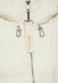 Nafouknutá bílá bunda s centrálním zipem, nastavitelnými šňůrkami s černými a oranžovými akcenty a štítkem s nápisem "Street One."