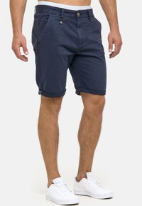 Shorts bleu marine en coton avec une coupe droite, des revers roulés et deux poches avant. Comprend une fermeture par bouton et une ceinture avec un accent.