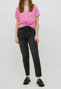 Růžový pletený top s krátkým rukávem a zkrouceným předním dílem, spárovaný s černými džínami s vysokým pasem a černými slip-on botami se zlatými akcenty.