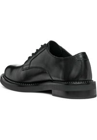 Chaussure habillée en cuir noir avec une finition lisse, bout arrondi et détails cousus le long de la semelle. Dotée d'un talon en caoutchouc à profil bas.