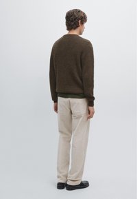 Brown textured knit sweater paired with light beige corduroy pants. Simple design with a crew neck and long sleeves, featuring a dark green accent.