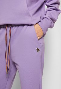 Levandulová mikina se klokaní kapsou, s vícerozbarvenou šňůrkou a malým vyšitým detailem koně na pase.