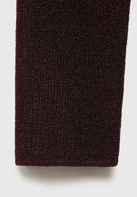 Gros plan d'un tissu tricoté texturé bordeaux foncé avec un motif dense de mailles bouclées sur un fond clair.