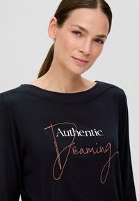 Zwarte langarmshirt met ronde halslijn, met als opvallende details witte "Authentic" en roze cursieve "Dreaming" tekst.