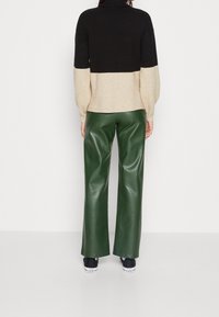 Schwarz- und cremefarbener Farbblock-Pullover mit hohem Kragen, überschnittenen Ärmeln und weiten, grünen Hosen aus Kunstleder. Dazu schwarze Sneakers.