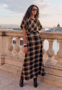 Abito lungo in fantasia scozzese multicolore, con maniche corte a sbuffo, vestibilità morbida e tasche laterali. Abbinato a stivali scuri con punta affusolata.