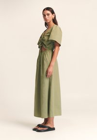 Zelen komplet sestavljen iz zgornjega dela z zavezovanjem spredaj in kratkimi rokavi ter dolge, tekoče krilo. Črni ravni sandali dopolnjujejo videz.