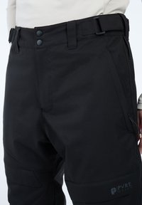 Zwarte outdoorbroek met een gladde textuur, voorzien van een knoopsluiting, verstelbare taille en cargozakken aan de voorkant en zijkanten.