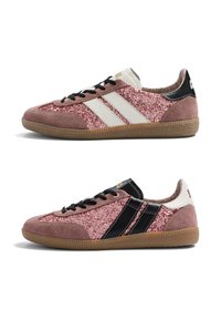 Paire de baskets roses pailletées avec des accents en suède et semelles en gomme, avec des rayures blanches sur une chaussure et des rayures noires sur l'autre.